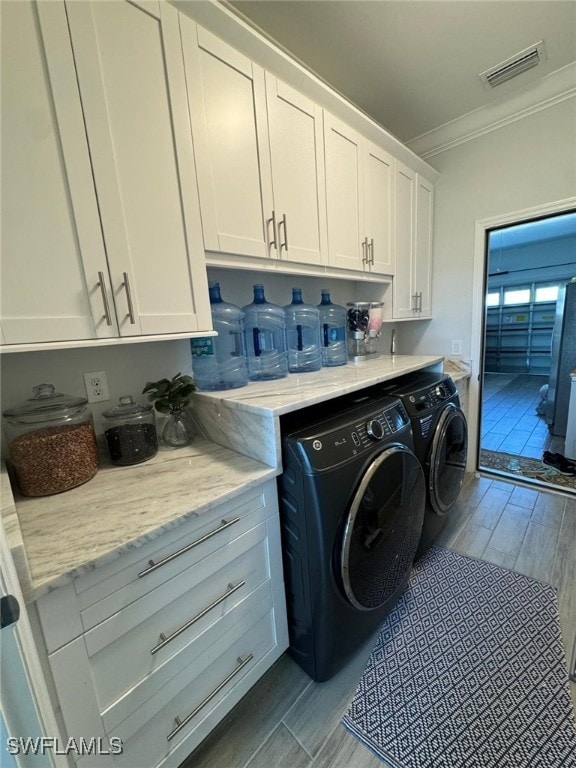 clothes washing area with cabinets, light wood-type flooring, separate washer and dryer, and crown molding