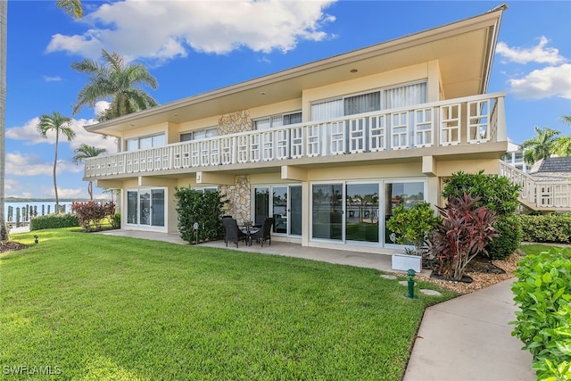 rear view of property featuring a yard, a balcony, a water view, and a patio