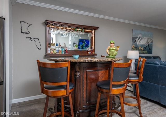 bar with wood-type flooring, ornamental molding, and stainless steel refrigerator