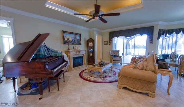 living room featuring ceiling fan, a raised ceiling, ornamental molding, and light tile patterned floors