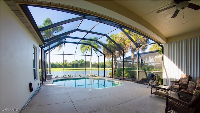 view of pool with a lanai, ceiling fan, a water view, and a patio