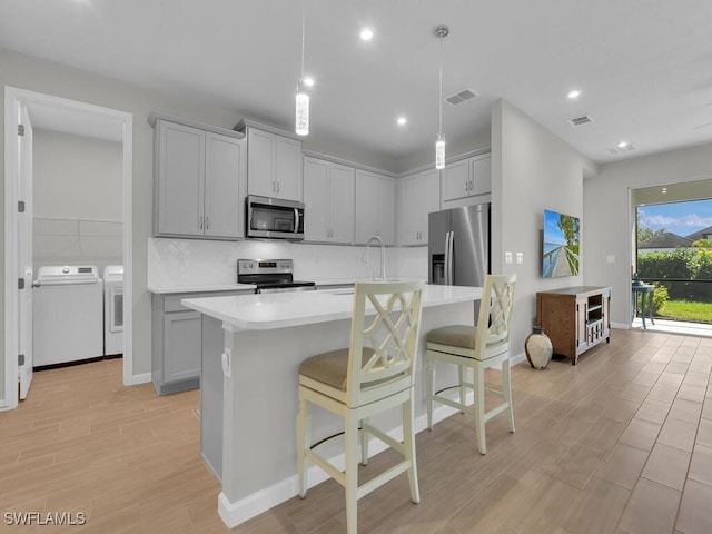 kitchen with hanging light fixtures, washer and dryer, gray cabinets, a kitchen bar, and stainless steel appliances