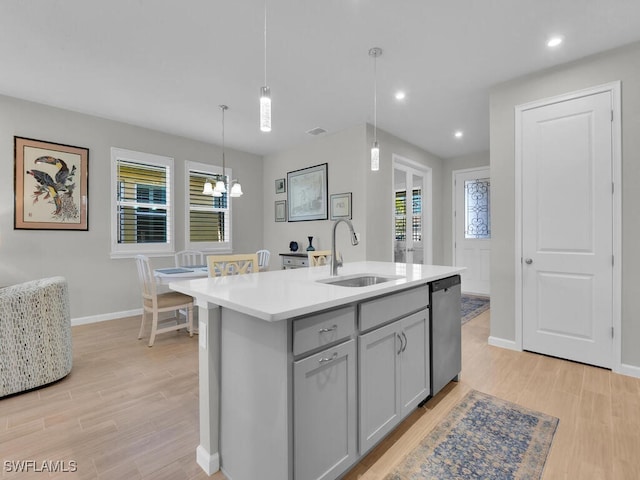 kitchen featuring dishwasher, a center island with sink, sink, gray cabinets, and light hardwood / wood-style floors