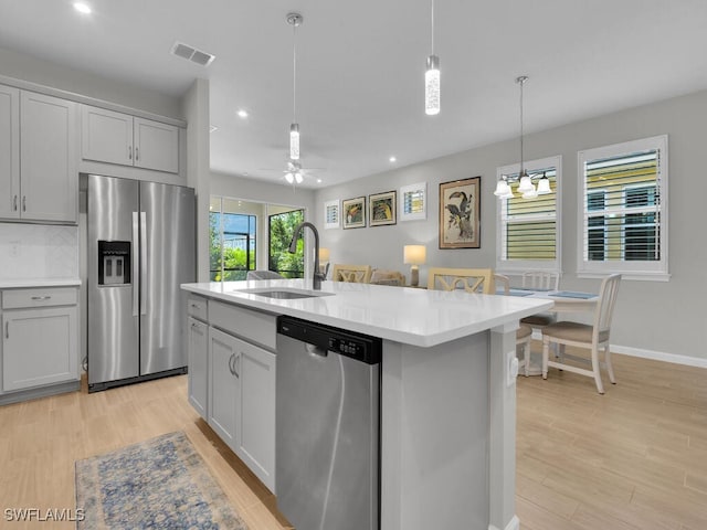 kitchen featuring a kitchen island with sink, ceiling fan with notable chandelier, sink, light hardwood / wood-style flooring, and appliances with stainless steel finishes