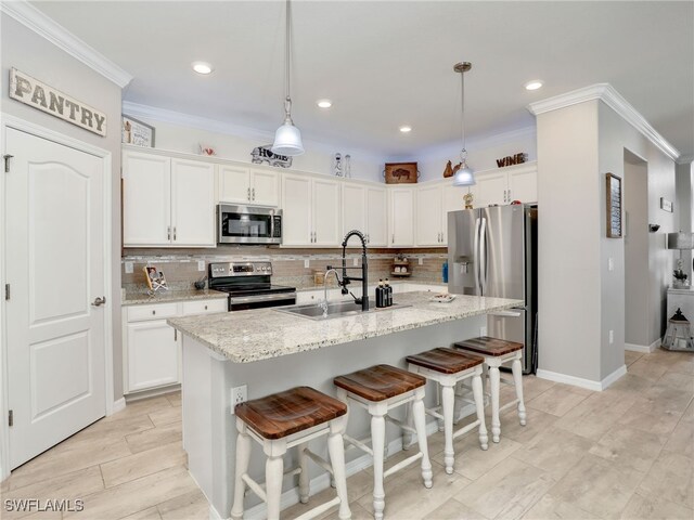 kitchen with light stone countertops, pendant lighting, appliances with stainless steel finishes, an island with sink, and sink