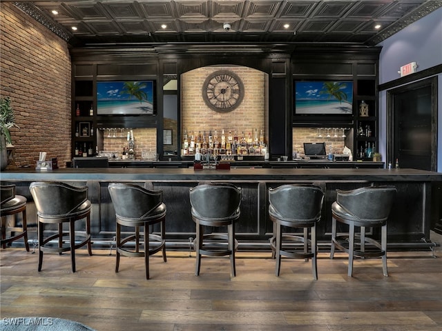 bar featuring a community bar, an ornate ceiling, brick wall, and hardwood / wood-style flooring