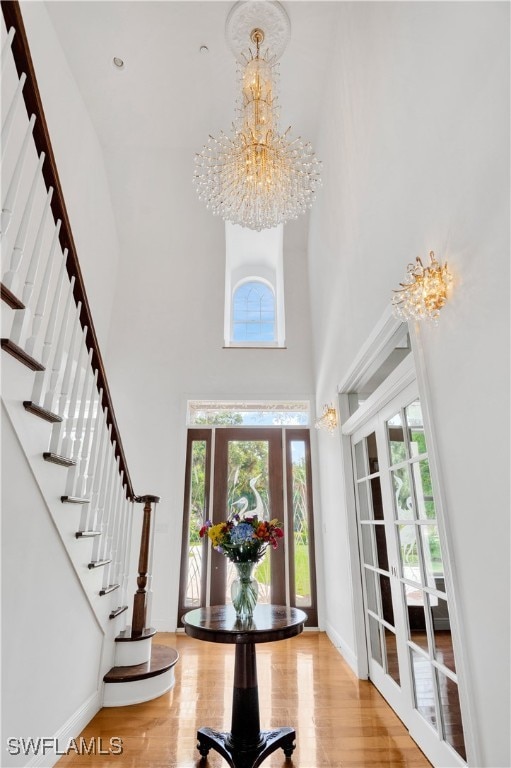 entrance foyer with hardwood / wood-style floors, a towering ceiling, an inviting chandelier, and french doors