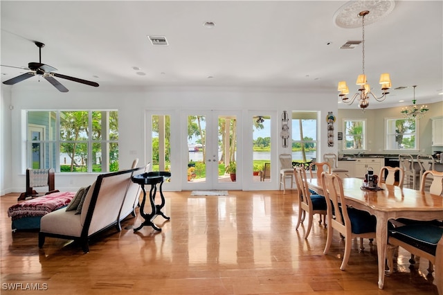 dining space with ceiling fan with notable chandelier, french doors, and light hardwood / wood-style flooring