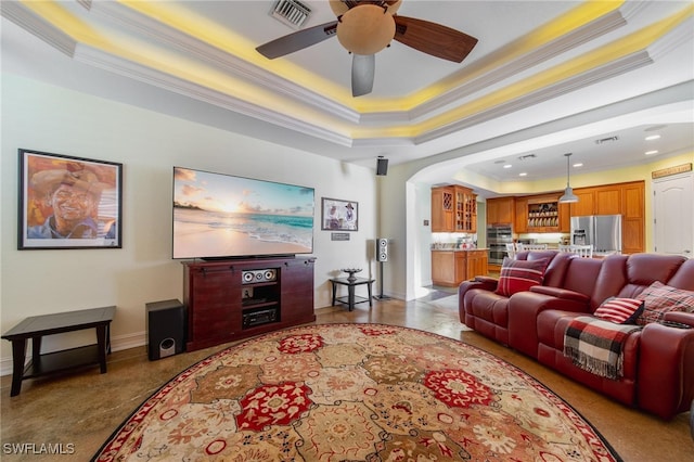 living room with a raised ceiling, ceiling fan, and ornamental molding