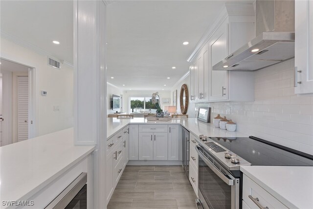 kitchen featuring stainless steel electric range, white cabinets, wall chimney exhaust hood, decorative backsplash, and kitchen peninsula