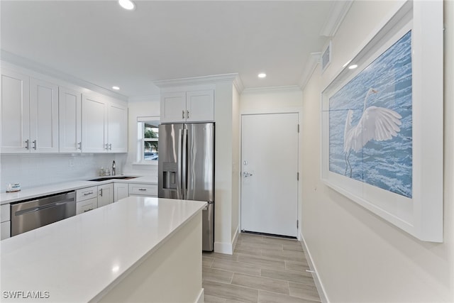 kitchen featuring appliances with stainless steel finishes, tasteful backsplash, ornamental molding, sink, and white cabinetry