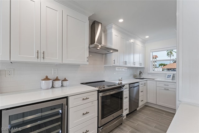 kitchen with sink, wall chimney exhaust hood, beverage cooler, white cabinets, and appliances with stainless steel finishes