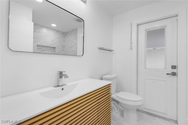 bathroom featuring a tile shower, vanity, and toilet