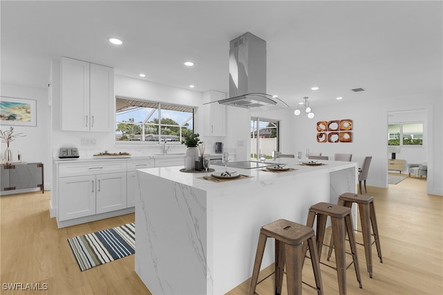 kitchen with light wood-type flooring, island range hood, white cabinetry, and a kitchen island