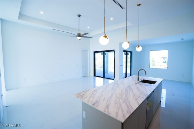 kitchen featuring a raised ceiling, sink, an island with sink, and a healthy amount of sunlight