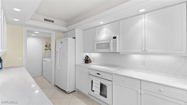 kitchen with white appliances, washing machine and dryer, light stone countertops, light tile patterned floors, and white cabinetry