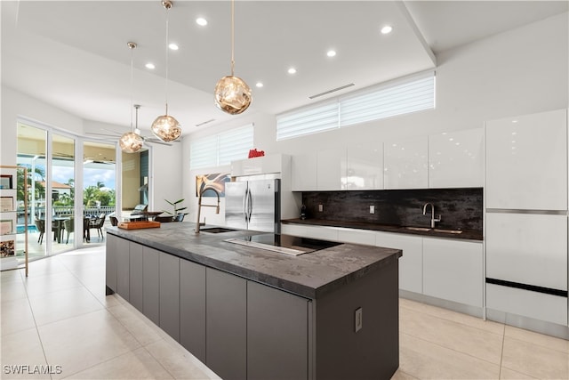 kitchen featuring a large island with sink, stainless steel fridge, pendant lighting, decorative backsplash, and white cabinets