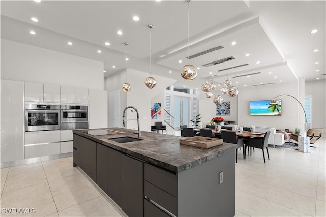 kitchen featuring white cabinetry, sink, hanging light fixtures, a large island with sink, and light tile patterned flooring