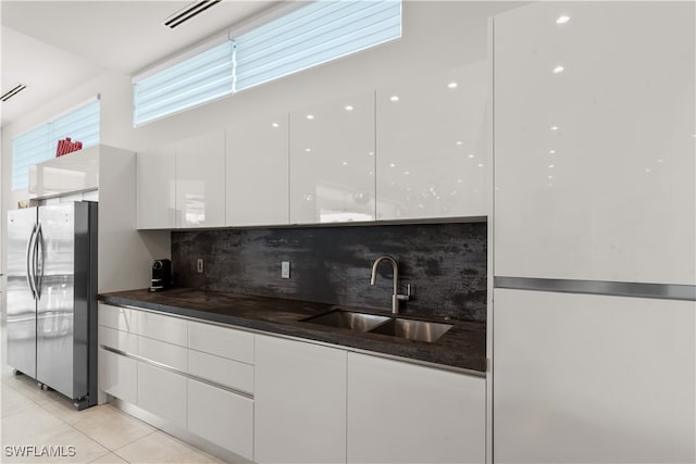 kitchen featuring stainless steel refrigerator, white cabinetry, sink, backsplash, and light tile patterned floors