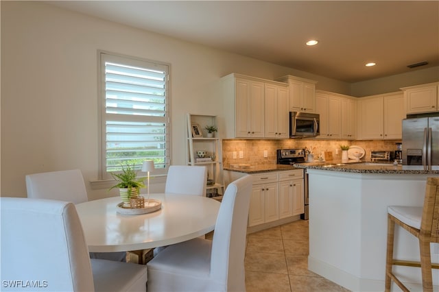 kitchen featuring decorative backsplash, appliances with stainless steel finishes, white cabinetry, and dark stone counters