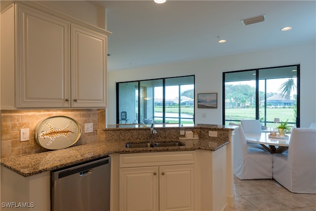 kitchen featuring white cabinets, sink, stainless steel dishwasher, dark stone countertops, and light tile patterned floors