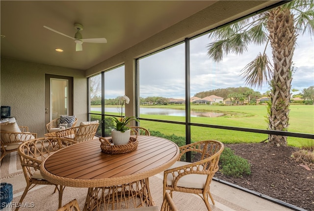 sunroom with ceiling fan and a water view