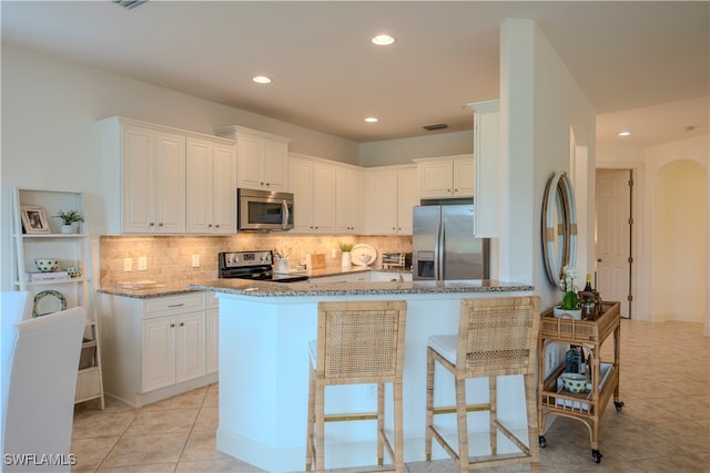 kitchen with stainless steel appliances, a kitchen island, light tile patterned floors, stone counters, and white cabinetry