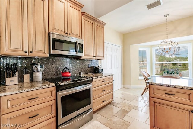 kitchen with appliances with stainless steel finishes, backsplash, an inviting chandelier, and light stone counters