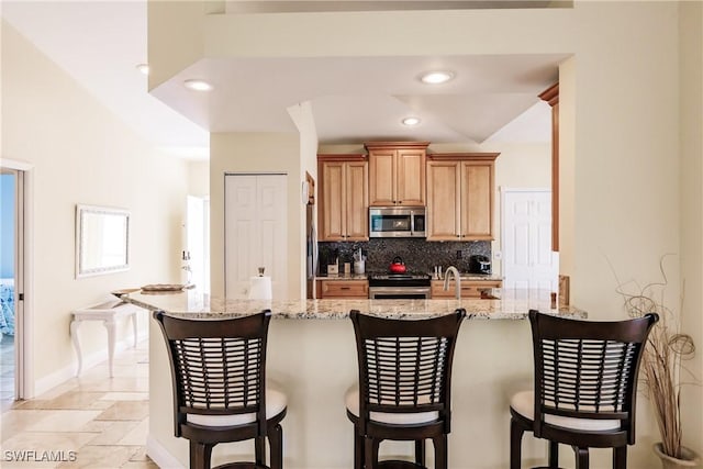 kitchen with kitchen peninsula, backsplash, light stone counters, stainless steel appliances, and a breakfast bar area