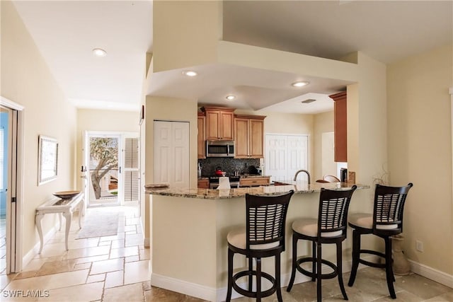 kitchen featuring backsplash, a kitchen breakfast bar, light stone countertops, appliances with stainless steel finishes, and kitchen peninsula