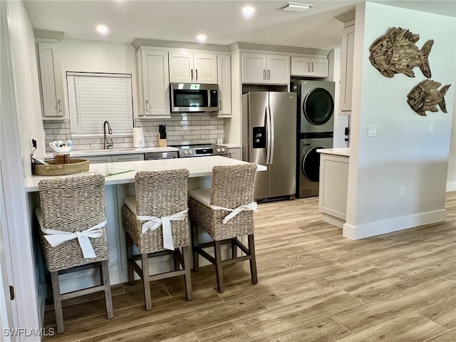 kitchen featuring stainless steel appliances, sink, light hardwood / wood-style flooring, white cabinetry, and stacked washer / drying machine