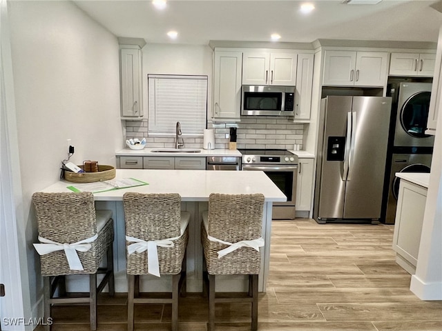 kitchen featuring sink, a breakfast bar area, appliances with stainless steel finishes, tasteful backsplash, and stacked washer / dryer