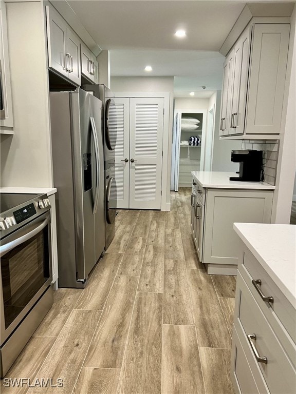 kitchen featuring appliances with stainless steel finishes, stacked washing maching and dryer, light hardwood / wood-style flooring, and gray cabinetry