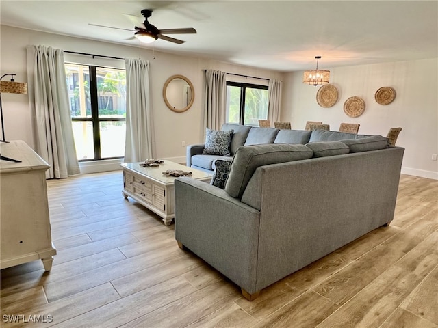 living room featuring ceiling fan with notable chandelier and light wood-type flooring