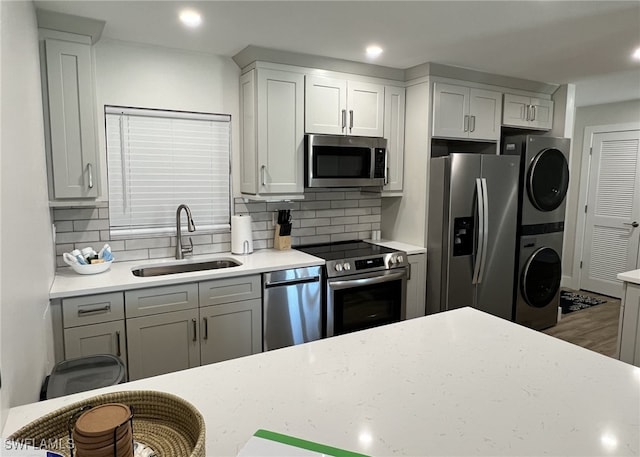 kitchen with stacked washer / dryer, decorative backsplash, sink, and stainless steel appliances