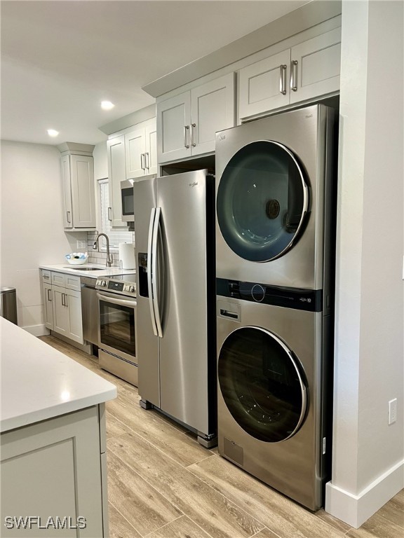 kitchen with white cabinetry, sink, light hardwood / wood-style floors, stacked washer and clothes dryer, and appliances with stainless steel finishes