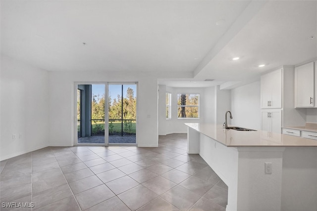 kitchen featuring white cabinets, light tile patterned flooring, a kitchen island with sink, and sink