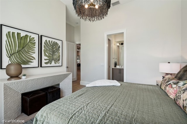 bedroom featuring a towering ceiling, wood-type flooring, connected bathroom, and a chandelier