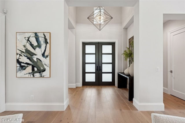 entrance foyer featuring french doors, light hardwood / wood-style flooring, and a notable chandelier