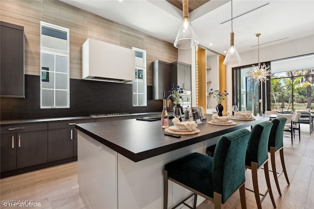 kitchen featuring dark brown cabinets, light wood-type flooring, an inviting chandelier, and exhaust hood