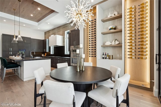 dining area with a tray ceiling, a chandelier, sink, and light hardwood / wood-style floors