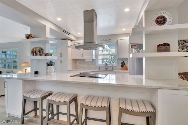 kitchen with open shelves, stovetop, island range hood, white cabinetry, and a sink