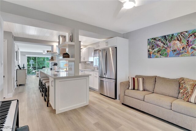 kitchen featuring sink, stainless steel refrigerator, white cabinetry, a kitchen breakfast bar, and a kitchen island