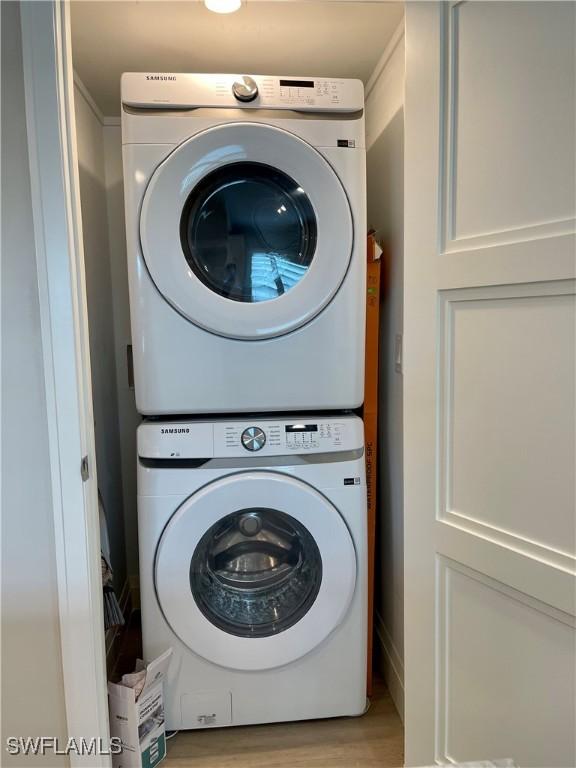 laundry room featuring stacked washing maching and dryer and light hardwood / wood-style flooring