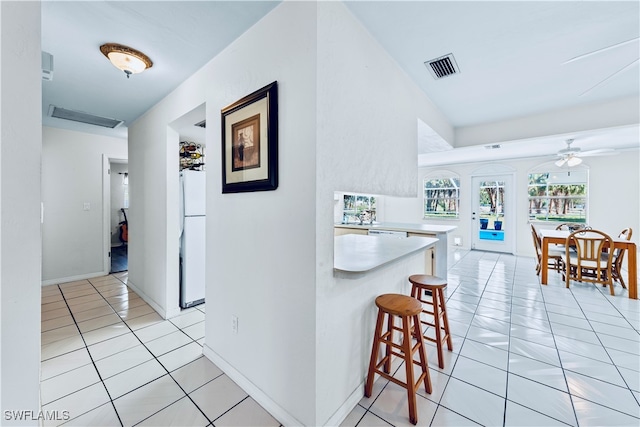 kitchen with ceiling fan, white fridge, light tile patterned flooring, and a breakfast bar area