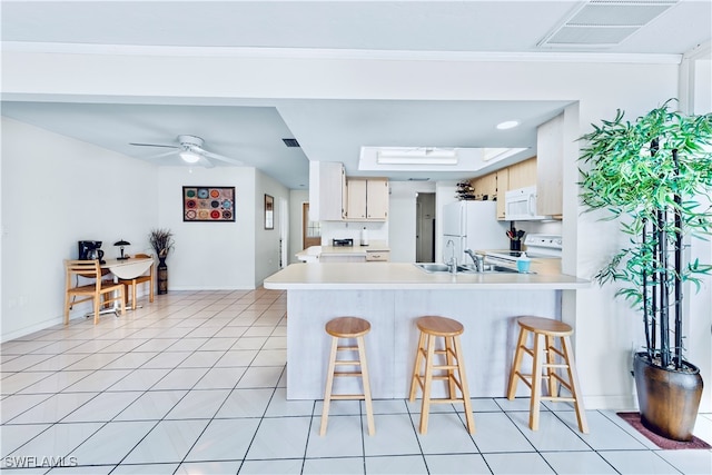 kitchen with a kitchen bar, kitchen peninsula, light tile patterned floors, and white appliances