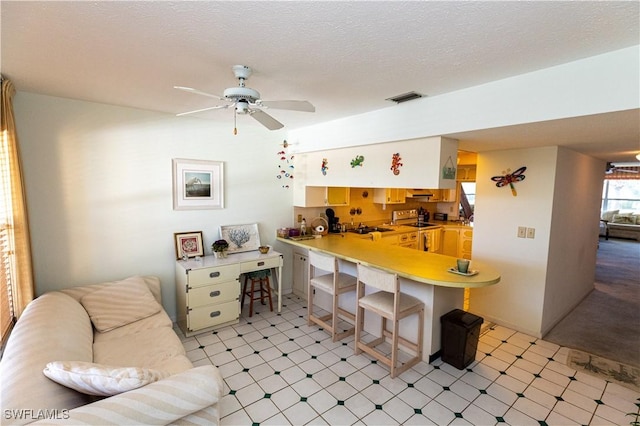 kitchen featuring a peninsula, electric range, visible vents, open floor plan, and a kitchen bar