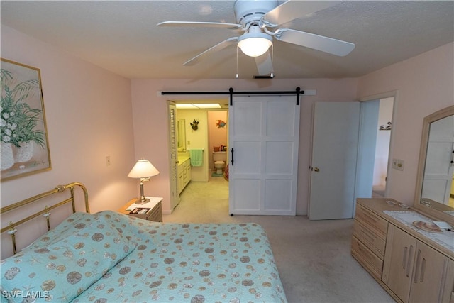 bedroom with a ceiling fan, light carpet, ensuite bathroom, and a barn door