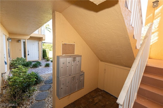 interior space with mail area, vaulted ceiling, a textured ceiling, and a textured wall