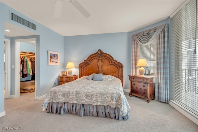 bedroom with ceiling fan, light colored carpet, a walk in closet, and a closet